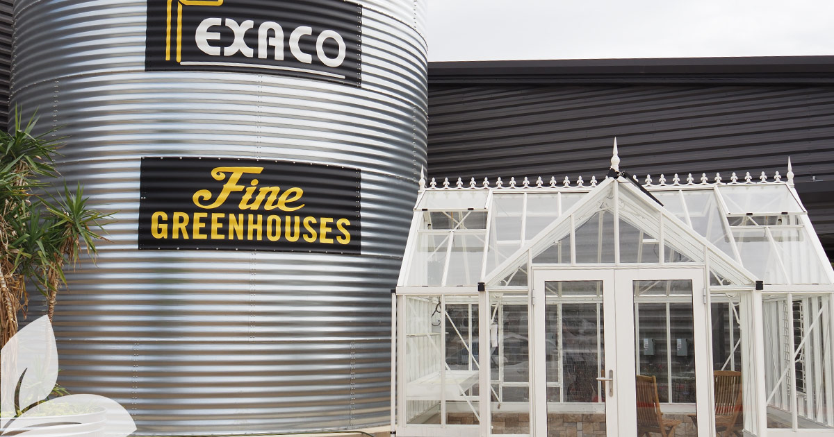 White greenhouse (orangerie) in front of Exaco logo on their showroom building