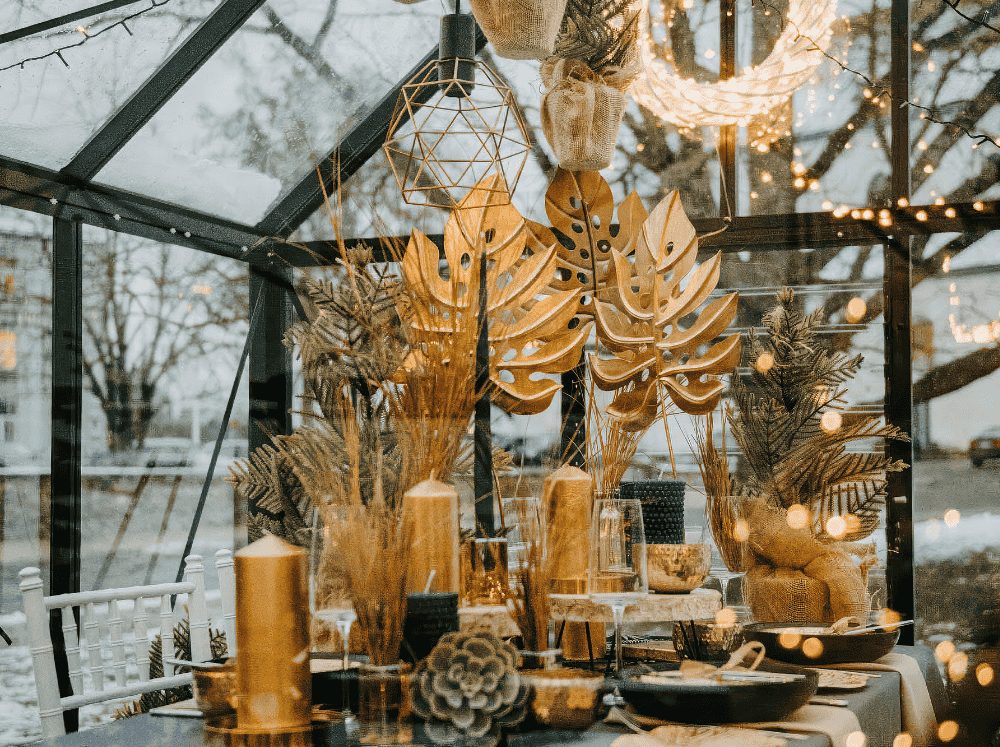 Rustic green and gold holiday dining table inside of a greenhouse